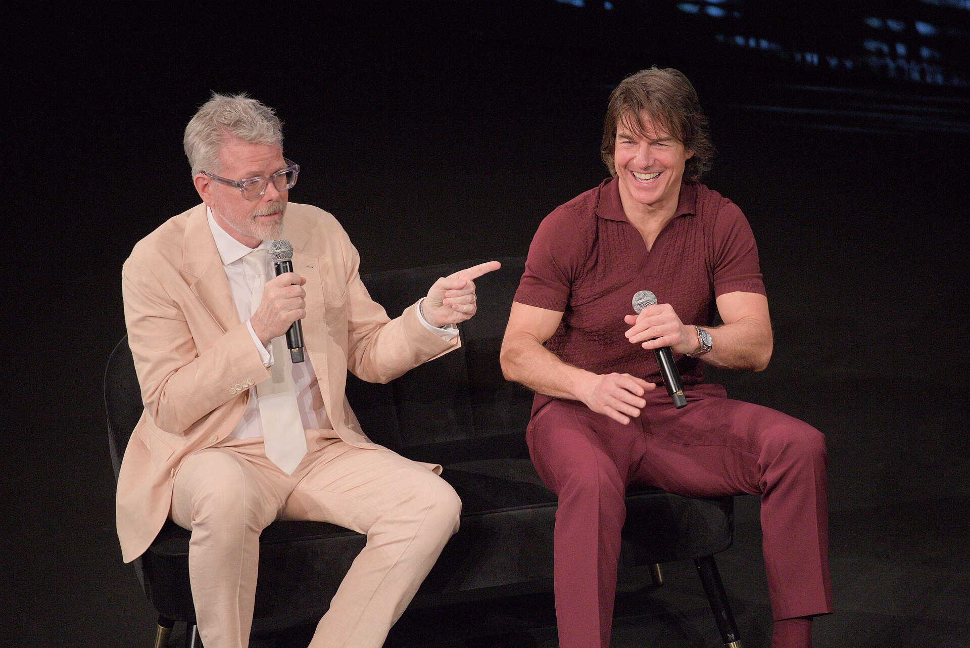 Christopher McQuarrie points toward Tom Cruise as both hold microphones during a 2025 Cannes question-and-answer session for Mission: Impossible — The Final Reckoning.